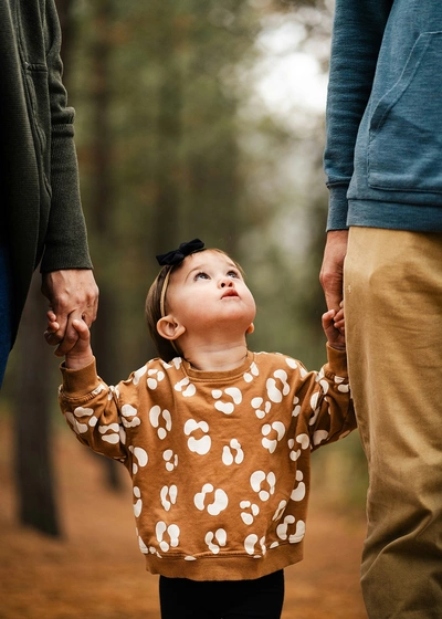 Bilde av et lite barn som holder to voksenpersoner i hendene. Barnet ser opp mot den ene voksne.