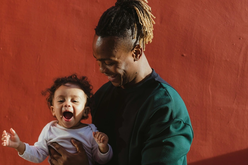 Bilde av en smilende mann som holder et leende barn i armene. 